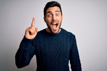 Young handsome man with beard wearing casual sweater standing over white background pointing finger...