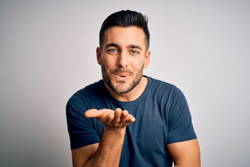 Young handsome man wearing casual t-shirt standing over isolated white background looking at the camera blowing a kiss with hand on air being lovely and sexy. Love expression.