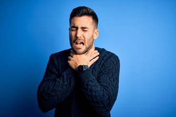 Young handsome man wearing casual sweater standing over isolated blue background shouting suffocate because painful strangle. Health problem. Asphyxiate and suicide concept.