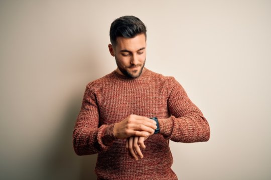 Young handsome man wearing casual sweater standing over isolated white background Checking the time on wrist watch, relaxed and confident
