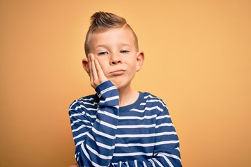 Young little caucasian kid with blue eyes wearing nautical striped shirt over yellow background thinking looking tired and bored with depression problems with crossed arms.