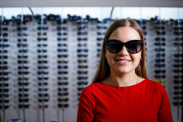 Beautiful young girl chooses sunglasses in an optics store.