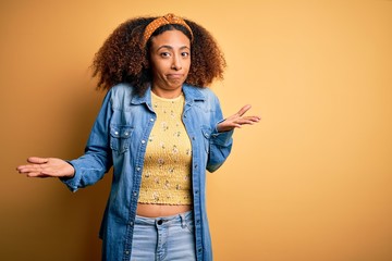 Beautiful african american with afro hair standing over yellow isolated background clueless and...