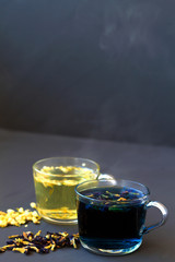 Healthy lifestyle. glass cups of blue and yellow herbal tea on a black background. Hot butterfly pea tea and Jasmine tea. Hot drinks. two cups of hot tea with dry flowers on a black table. vertical