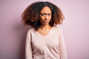 Young african american woman with afro hair wearing casual sweater over pink background skeptic and nervous, frowning upset because of problem. Negative person.