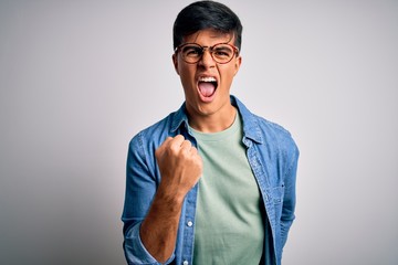 Young handsome man wearing casual shirt and glasses over isolated white background angry and mad raising fist frustrated and furious while shouting with anger. Rage and aggressive concept.