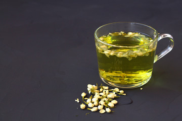 Healthy lifestyle. Jasmine tea. cup of hot herbal tea with dry flowers of Jasmine on a black table with copy space. Hot drinks. glass cup of Jasmine tea on a black background.