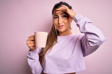 Young beautiful brunette woman drinking mug of coffee over isolated pink background stressed with hand on head, shocked with shame and surprise face, angry and frustrated. Fear and upset for mistake.