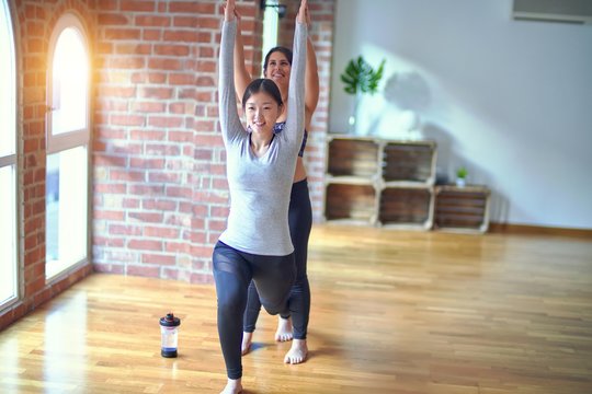 2 young beautiful sportswomen practicing yoga. One of them teaching warrior pose at gym