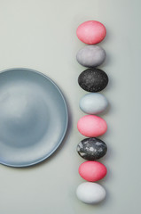 Line of colorful Easter eggs near blue plate on grey background. Minimalistic flat lay
