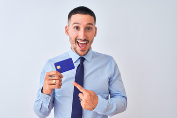 Young business man holding credit card over isolated background very happy pointing with hand and finger