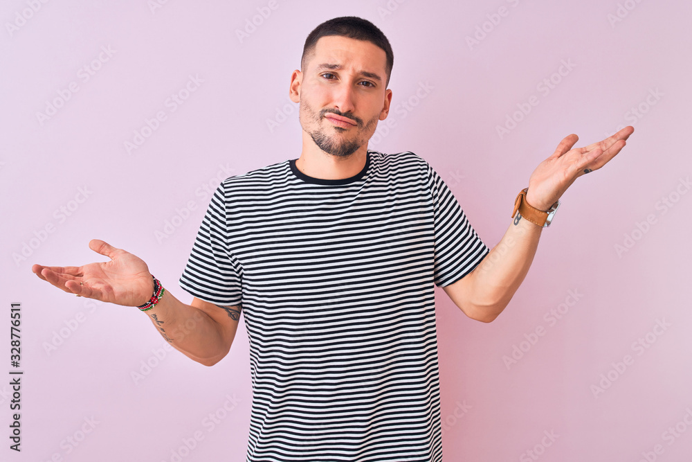 Sticker young handsome man wearing striped t-shirt standing over pink isolated background clueless and confu