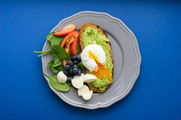 Wholesome tasty full of vitamins and health breakfast with avocado, berries, cheese and tomatoes with basil on classic blue background. Detox. Healthy food. Soft focus and beautiful bokeh.