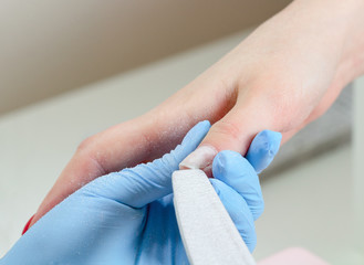 Manicurist smooths a fingernail with a nail file in beauty salon.