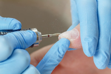 Manicurist polishing nail with electric milling cutter in a beauty salon. Manicure process