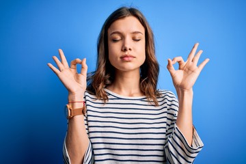 Young beautiful blonde girl wearing casual sweater standing over blue isolated background relax and smiling with eyes closed doing meditation gesture with fingers. Yoga concept.