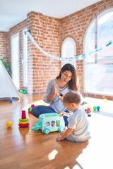 Beautiful teacher and toddler playing around lots of toys at kindergarten