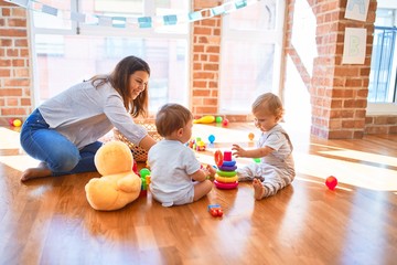 Beautiful teacher and toddlers playing around lots of toys at kindergarten