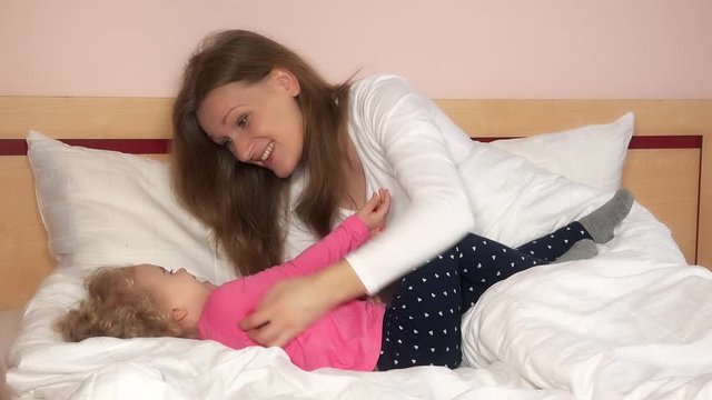 mother play with her daughter, tickles her hands and both laugh in bedroom. 4K