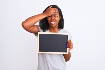 Young african american woman holding blank school blackboard over isolated background stressed with hand on head, shocked with shame and surprise face, angry and frustrated. Fear and upset
