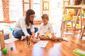 Beautiful teacher and toddler drawing using pencils and paper around lots of toys at kindergarten