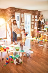 Beautiful teacher and toddler playing basketball using ball and wicker basket around lots of toys at kindergarten