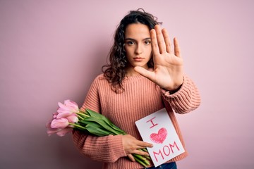 Beautiful curly hair woman holding love mom message and tulips celebrating mothers day with open hand doing stop sign with serious and confident expression, defense gesture