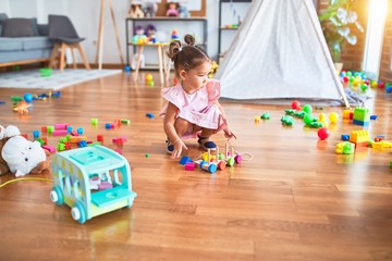 Young beautiful toddler sitting on the floor playing with wooden train toy at kindergaten