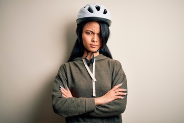 Young beautiful chinese woman wearing bike helmet over isolated white background skeptic and nervous, disapproving expression on face with crossed arms. Negative person.