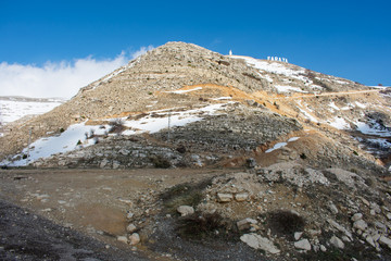 Lebanon mountain village Faraya. Village sign with Saint Charbel statue and cross on the mountain top
