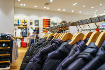 Modern fashion store. Buyers choose clothes. Shirts, hoodies, blouses and half-sweaters, a sweater on a hanger in a clothing store close-up. Sale and shopping in stores. Soft focus.