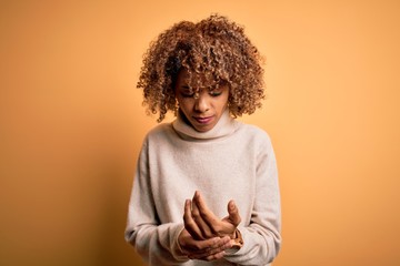 Obraz na płótnie Canvas Young beautiful african american woman wearing turtleneck sweater over yellow background Suffering pain on hands and fingers, arthritis inflammation