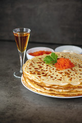 Tasty homemade pancakes close-up with red caviar and sour cream, a delicious snack for brandy glasses