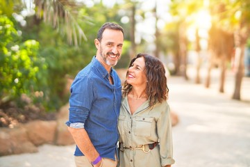 Fototapeta premium Middle age beautiful couple smiling happy and confident at town park. Standing with smile on face and hugging