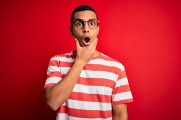 Young handsome african american man wearing casual striped t-shirt and glasses Looking fascinated with disbelief, surprise and amazed expression with hands on chin