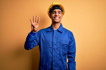 Young handsome african american worker man wearing blue uniform and security helmet showing and pointing up with fingers number four while smiling confident and happy.