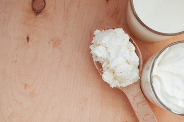 Cottage cheese on a wooden spoon, a glass of milk and sour cream. Rustic dairy products. Eco products. Healthy food.