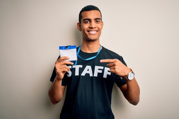 Young handsome african american worker man wearing staff uniform holding id card very happy pointing with hand and finger