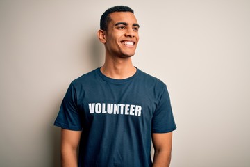 Young handsome african american man volunteering wearing t-shirt with volunteer message looking away to side with smile on face, natural expression. Laughing confident.