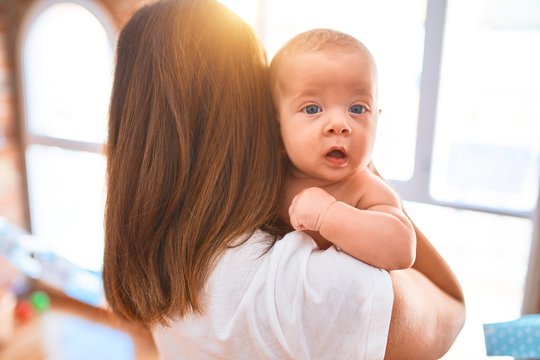 Young beautifull woman and her baby standing at home. Mother holding and hugging newborn