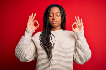 Young african american woman wearing casual winter sweater over red isolated background relax and smiling with eyes closed doing meditation gesture with fingers. Yoga concept.