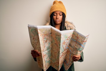 Fototapeta premium Young african american girl going on vacation holding turist city map over isolated background with a confident expression on smart face thinking serious