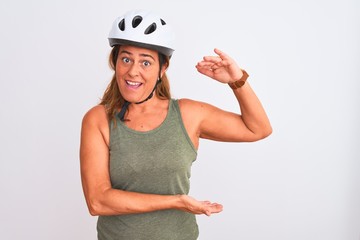 Middle age mature cyclist woman wearing safety helmet over isolated background gesturing with hands showing big and large size sign, measure symbol. Smiling looking at the camera. Measuring concept.