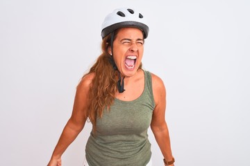 Middle age mature cyclist woman wearing safety helmet over isolated background angry and mad screaming frustrated and furious, shouting with anger. Rage and aggressive concept.