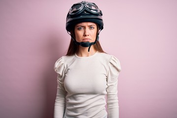 Young beautiful motorcyclist woman with blue eyes wearing moto helmet over pink background depressed and worry for distress, crying angry and afraid. Sad expression.