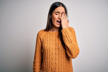 Young beautiful brunette woman wearing casual sweater over isolated white background Yawning tired covering half face, eye and mouth with hand. Face hurts in pain.