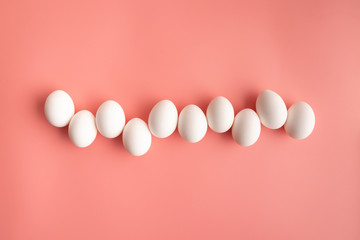 White chicken eggs arranged in a row on pastel pink backcground. Abstract Easter concept.