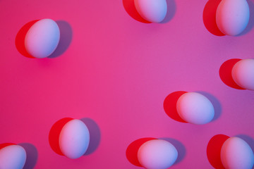 Red and blue color lights on white chicken eggs overhead view. Creative Easter concept.