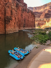 Two large motorized rafts on a beach in the Grand Canyon, with ropes in the sand and people walking...