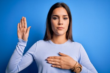 Young beautiful brunette woman wearing casual sweater standing over blue background Swearing with...